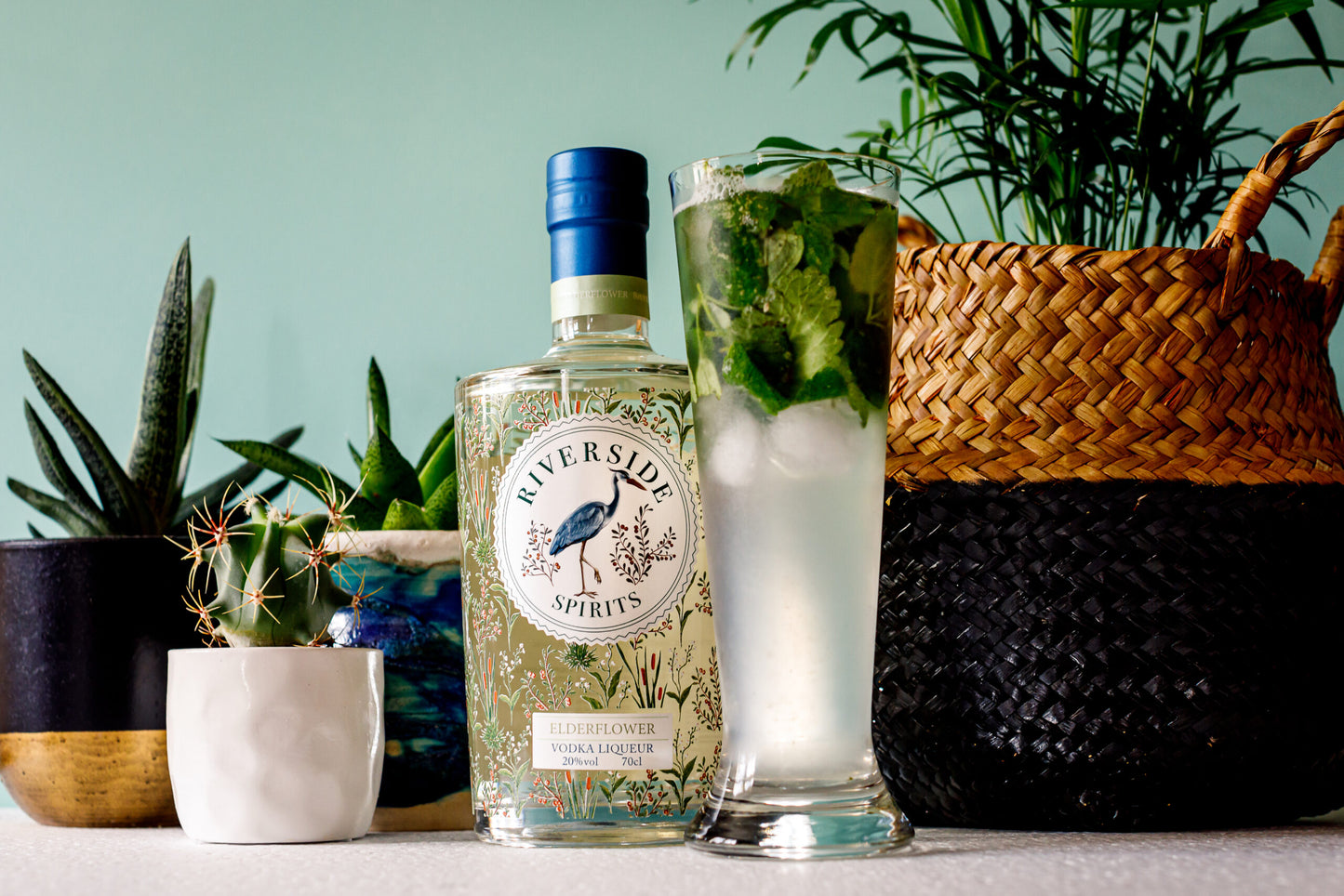 Bottle of Riverside Spirits Elderflower vodka liqueur with a glass of mojito and plants in the background