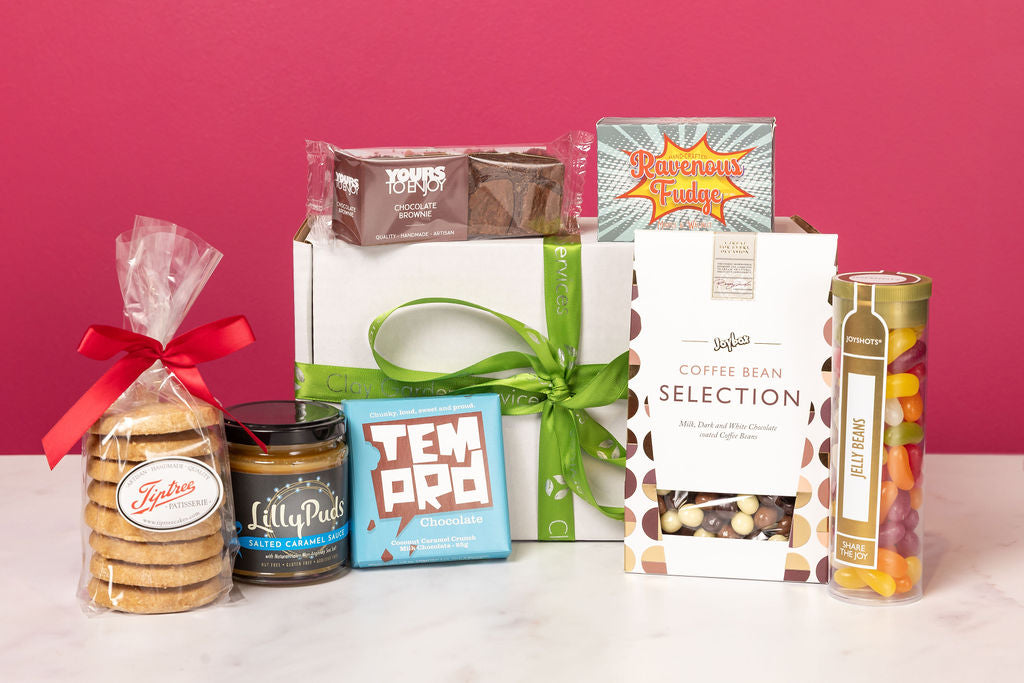The Stort Valley Gifting sweet treat box including: Assorted gift items including cookies, tea, and coffee beans on a pink background