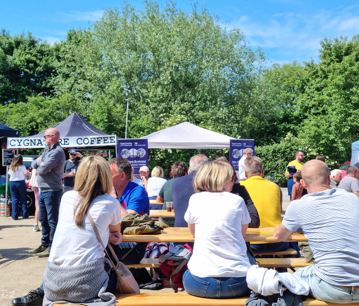 People sitting at outdoor tables with Stort Valley Gifting and other branded tents in the background