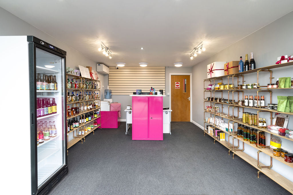 The Stort Valley Gifting Hamper Hub store interior with shelves stocked with products, a pink cabinet, and a refrigerator.