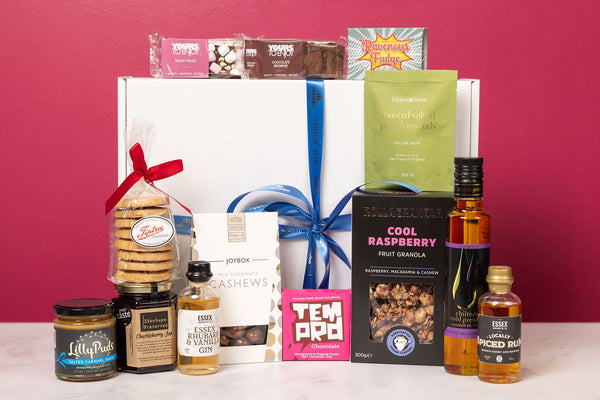 Personalised Stort Valley Gift basket with various items including snacks, drinks, and a box of chocolates against a pink background.