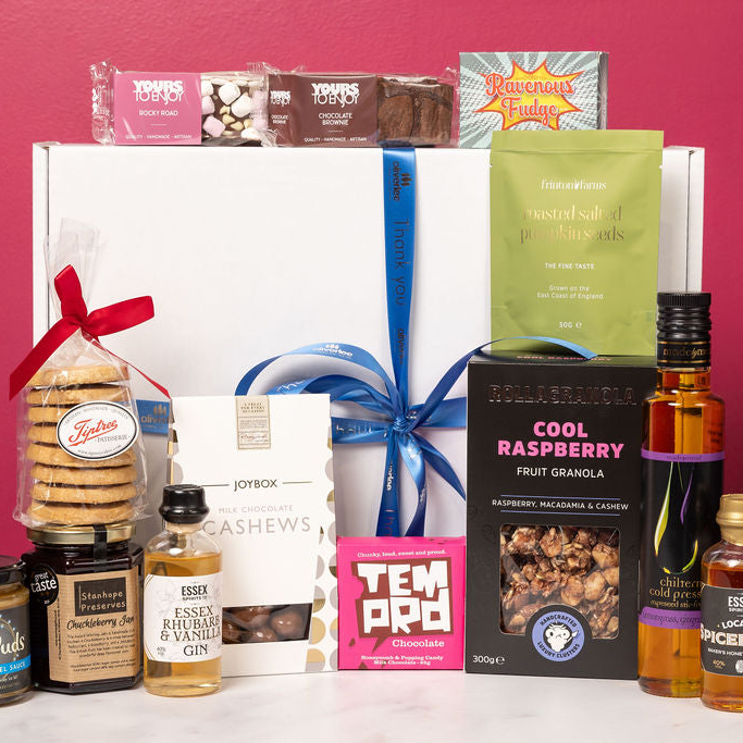 Stort Valley Gifting Hamper that includes: Assorted gourmet food and drink items including cookies, gin, and granola on a white surface with a pink background.