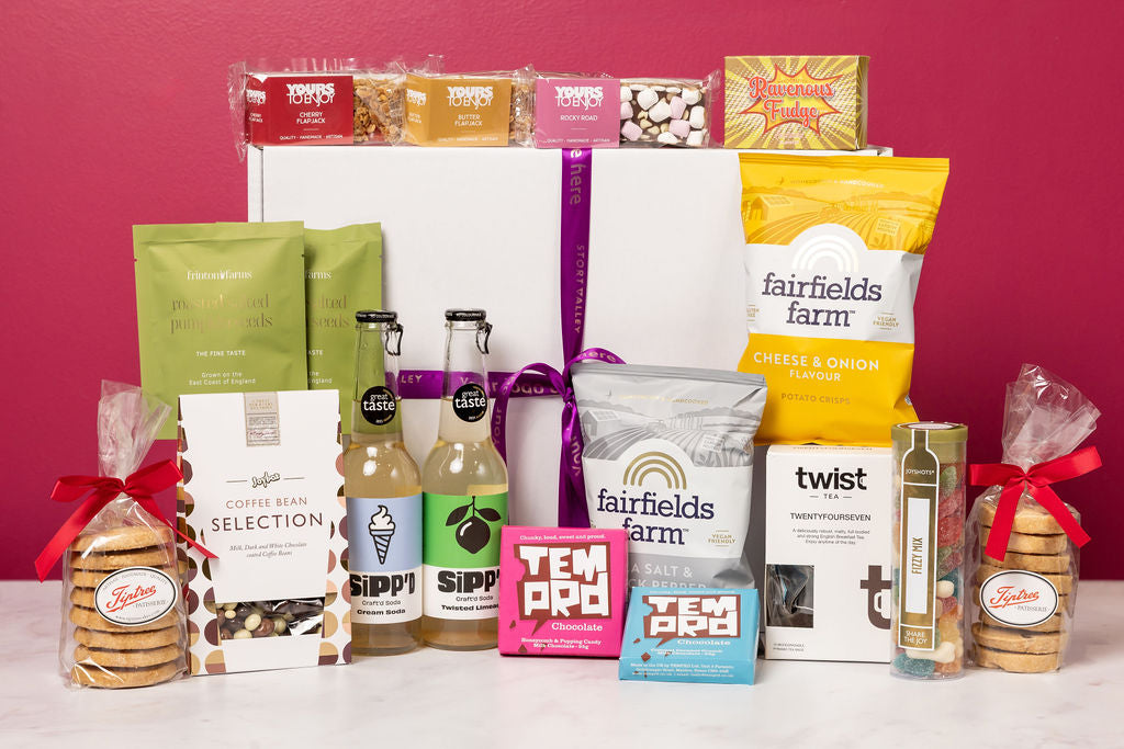 Stort Valley Gift box with assorted snacks and drinks arranged on a white surface with a pink background