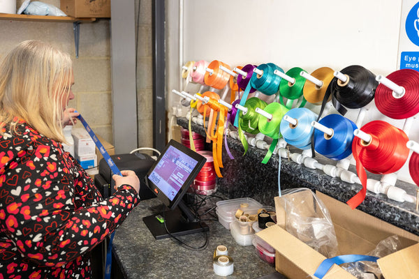 Stort Valley Gifting owner, Emma using a tablet with colourful spools of ribbon on a stand in the Hamper Hub
