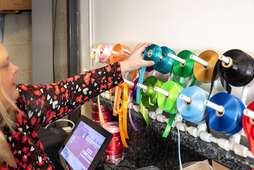 Emma Robson selecting a ribbon to customise for a hamper from a wall of ribbon choices at the Hamper Hub