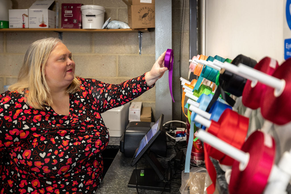 Emma Robson selecting a ribbon to customise for a hamper from a wall of ribbon choices at the Hamper Hub