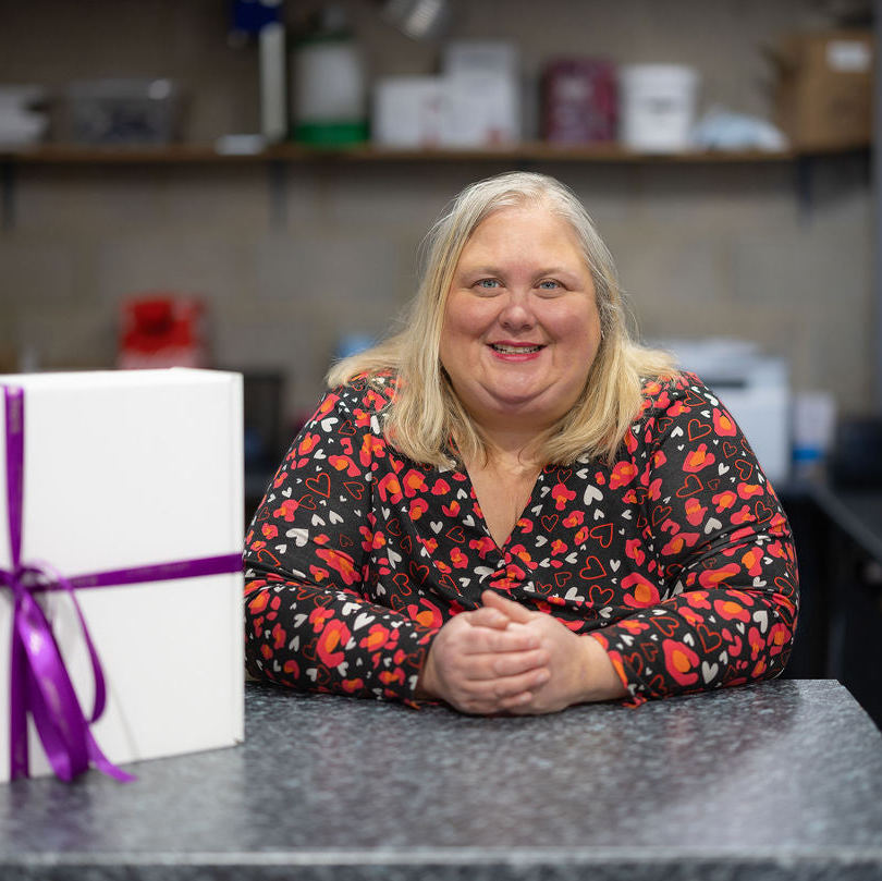 Emma Robson sitting at a counter with a Stort Valley ribboned gift box in the Hamper Hub