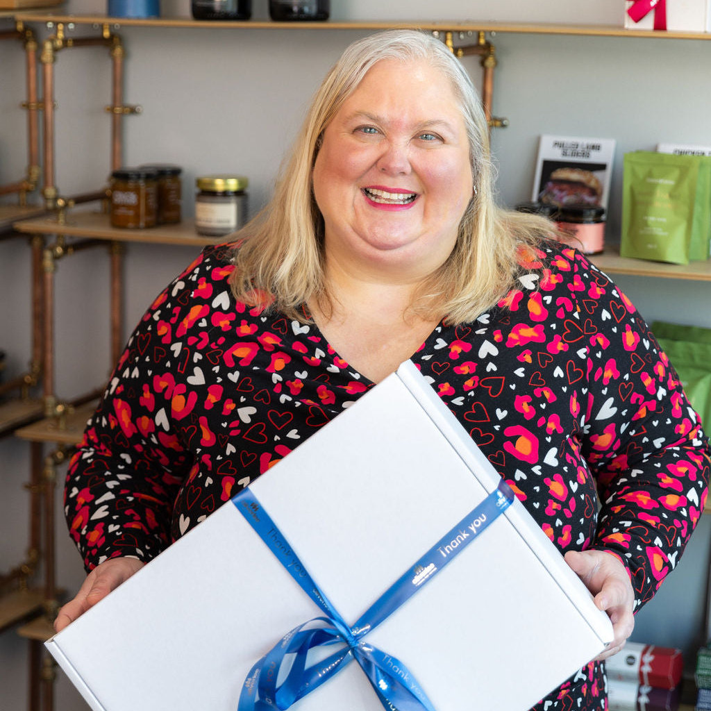Emma Robson holding a large Stort Valley gift box with a blue ribbon in the Hamper Hub