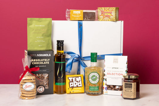 The Stort Valley Gifting celebration gift box including: Assorted food products including bottles, jars, and boxes on a white surface with a red background