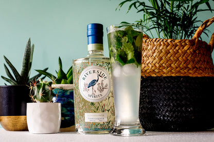 Bottle of Riverside Spirits Elderflower vodka liqueur with a glass of mojito and plants in the background