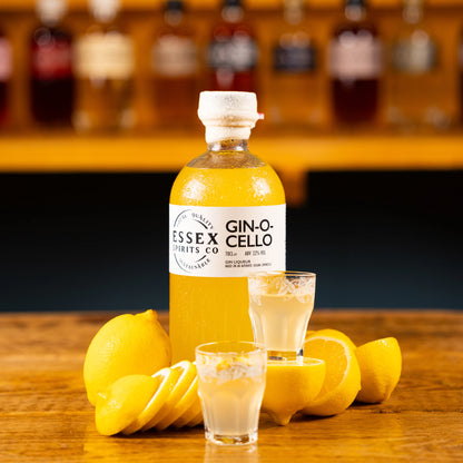 Bottle of Essex Spirits Co Gin-O-Cello with two glasses and lemons on a wooden surface available at Stort Valley Gifting