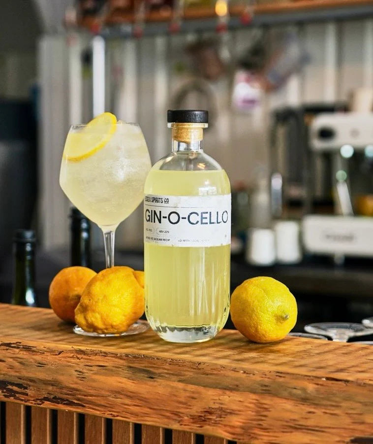 Bottle of Gin-O-Cello with a glass of lemonade and lemons on a bar counter available at Stort Valley Gifting