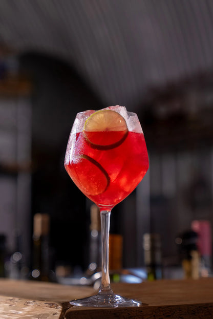 Red cocktail with ice cubes and a slice of fruit in a glass on a blurred bar background