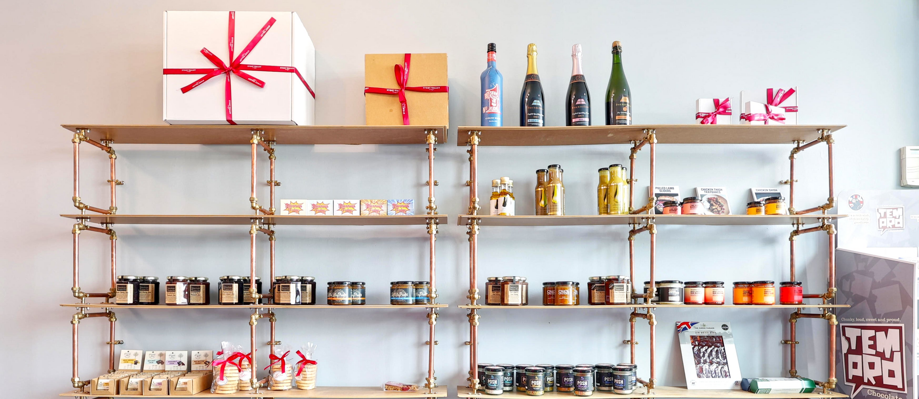 Shelving unit in the Stort Valley Gifting Hamper Hub with various items including bottles, jars and gift boxes against a light blue wall.