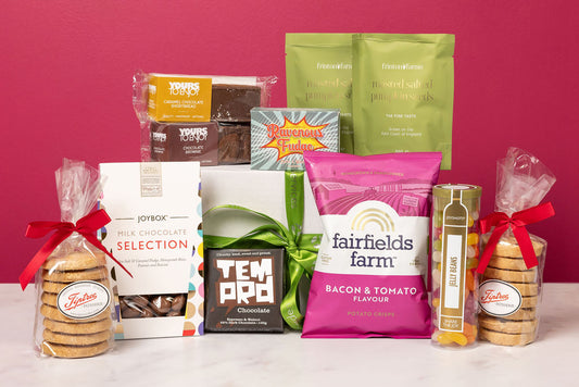 Assorted snacks and treats including cookies, chocolate bars, and packaged goods on a pink background