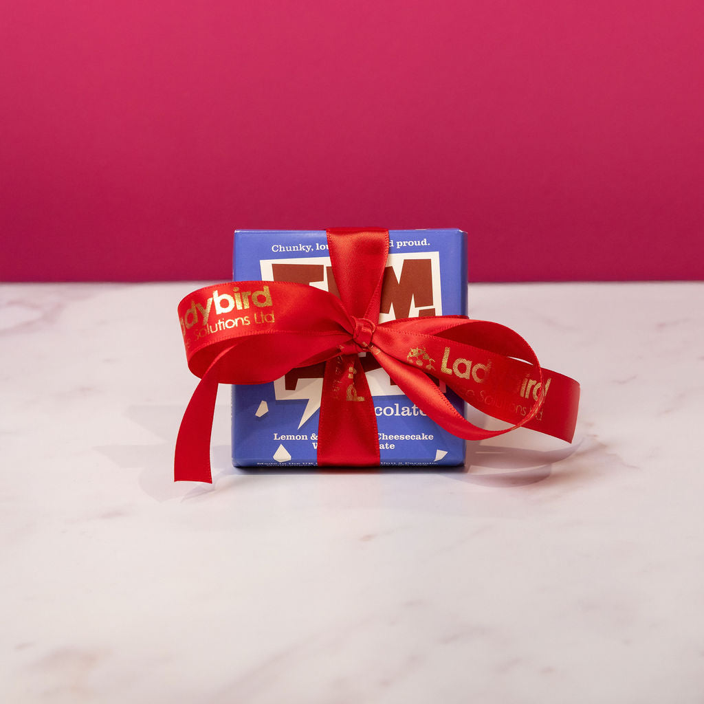 Temprd chocolate bar with a personalised Stort Valley red ribbon on a white surface against a pink background