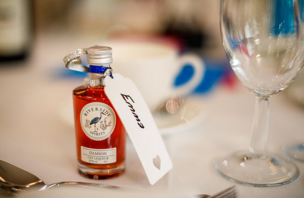 Miniature bottle of Riverside Spirits with a tag on a table with a glass and cutlery.